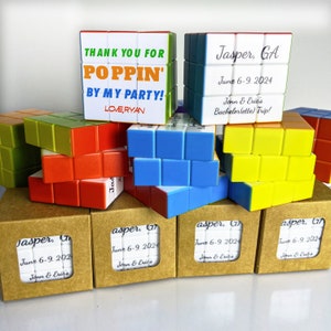 May include: A set of six small, colourful cube puzzles with personalised messages. The cubes are made of plastic and have a variety of colours, including red, blue, green, yellow, and white. The messages on the cubes include "Thank you for poppin' by my party! Love, Ryan" and "Jasper, GA June 6-9, 2024 Jenn & Eric's Bachelorette Trip!"
