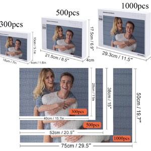 May include: Three different sizes of jigsaw puzzles featuring a couple. The puzzles are 300 pieces, 500 pieces, and 1000 pieces. The puzzles are white with a blue background and a picture of a couple in the centre. The couple are smiling and the man is holding the woman on his back. The puzzles are labelled with the number of pieces and the dimensions in inches and centimetres.