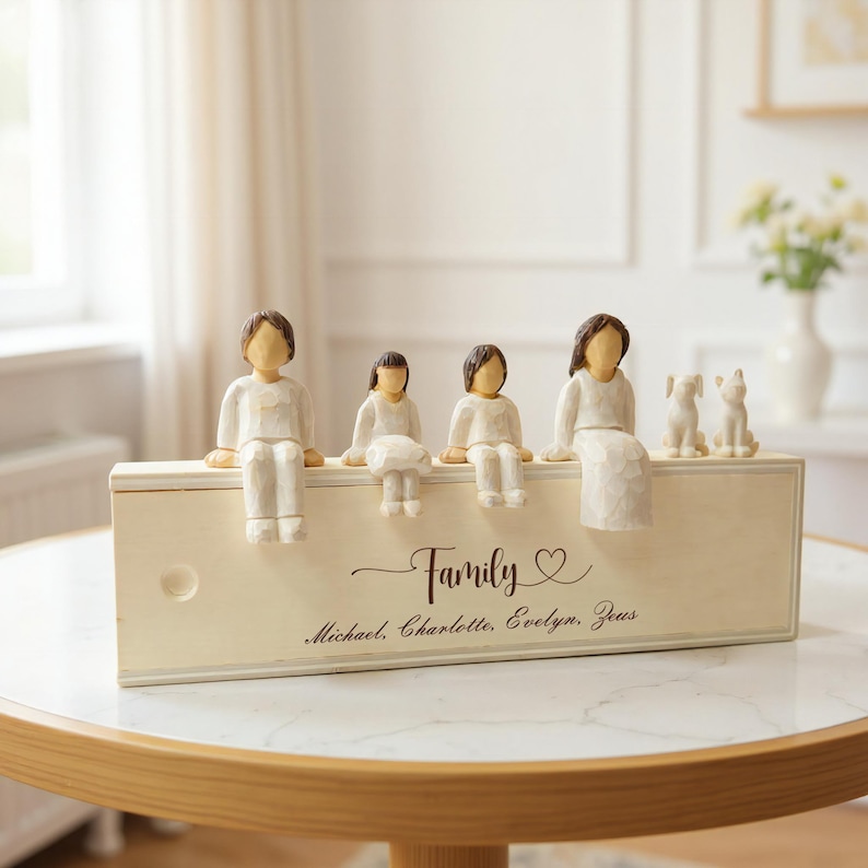 Może przedstawiać: Kremowa drewniana figurka rodziny z czterema postaciami i dwiema figurkami ps&oacute;w. Słowo "Family" jest napisane kursywą, wraz z imionami Michael, Charlotte, Evelyn i Zeus. Figurki siedzą na drewnianym pudełku.