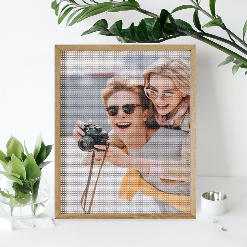 May include: A framed photo of two people smiling and taking a picture with a camera. The photo is in a wooden frame and the people are wearing sunglasses.