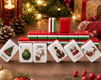 May include: A set of Christmas-themed mahjong tiles featuring festive illustrations including a tree, ornament, reindeer, nutcracker, snow globe, and Santa in a sleigh. The tiles have white faces with colorful graphics and red and green striped backs.