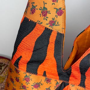 Pode incluir: Uma bolsa tote de patchwork com estampa de zebra preta e laranja, estampa floral laranja e estampa floral verde e laranja. A bolsa tem um formato triangular &uacute;nico.