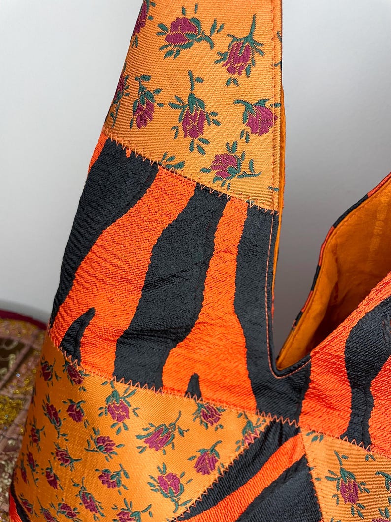 Pode incluir: Uma bolsa tote de patchwork com estampa de zebra preta e laranja, estampa floral laranja e estampa floral verde e laranja. A bolsa tem um formato triangular &uacute;nico.