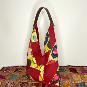 May include: A red, yellow and green patchwork tote bag with a brown leather strap. The bag is made from fabric scraps and has a unique, bohemian style.