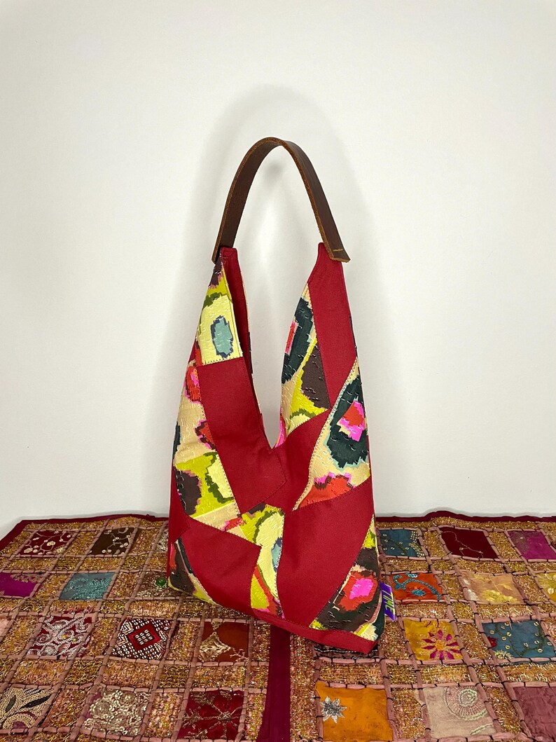 May include: A red, yellow and green patchwork tote bag with a brown leather strap. The bag is made from fabric scraps and has a unique, bohemian style.