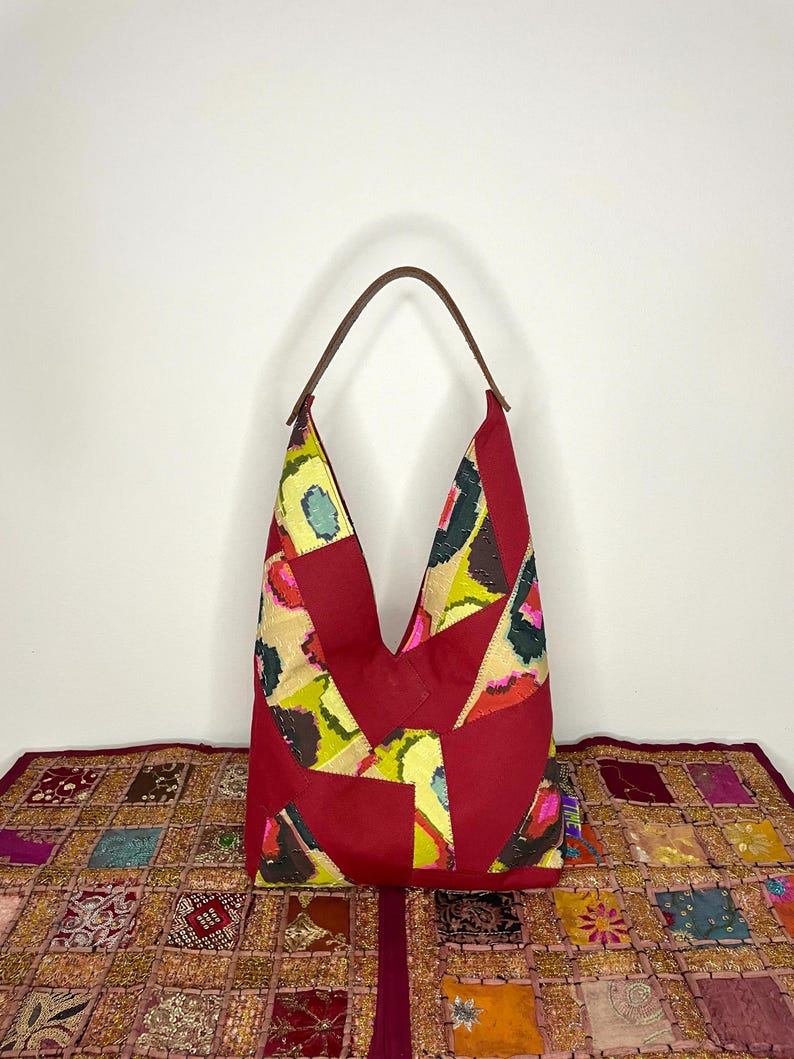 May include: A red patchwork tote bag with a brown leather handle. The bag features a geometric pattern with yellow, green, and pink accents.