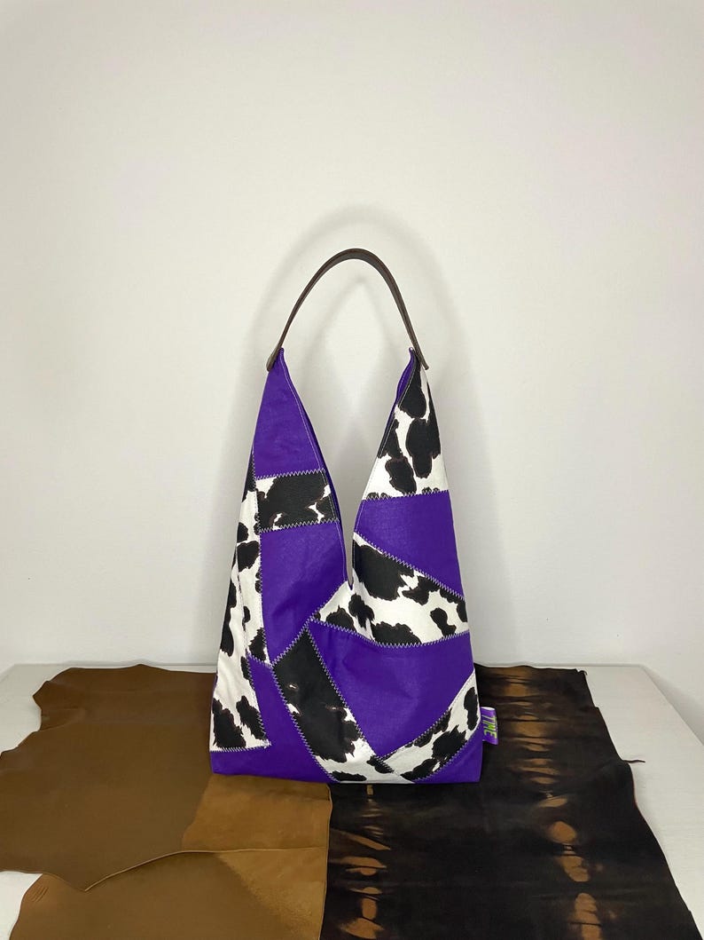 Op de afbeelding: Een patchwork tote bag in paars, zwart en wit met een bruin leren handvat.