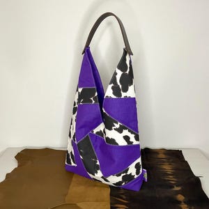 Op de afbeelding: Een paarse en zwarte patchwork tote bag met een koe-print ontwerp. De tas heeft een bruin leren handvat.