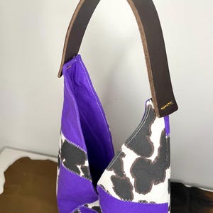 Op de afbeelding: Een paarse en witte patchwork tote bag met een bruin leren handvat. De tas heeft een geometrisch patroon met zwarte en witte vlekken.