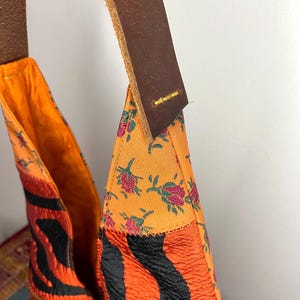 Pode incluir: Uma bolsa tote de patchwork laranja e preta brilhante com uma al&ccedil;a de couro marrom. A bolsa &eacute; feita de diferentes tecidos com padr&otilde;es florais e de zebra.