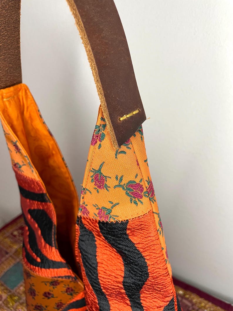 Pode incluir: Uma bolsa tote de patchwork laranja e preta brilhante com uma al&ccedil;a de couro marrom. A bolsa &eacute; feita de diferentes tecidos com padr&otilde;es florais e de zebra.