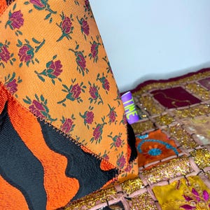 Pode incluir: Um close-up de um almofada de patchwork colorido com um padr&atilde;o floral e um padr&atilde;o de listras pretas e laranja. A almofada est&aacute; sentada em um tapete de patchwork colorido com acentos dourados.