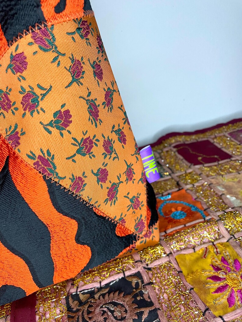 Pode incluir: Um close-up de um almofada de patchwork colorido com um padr&atilde;o floral e um padr&atilde;o de listras pretas e laranja. A almofada est&aacute; sentada em um tapete de patchwork colorido com acentos dourados.