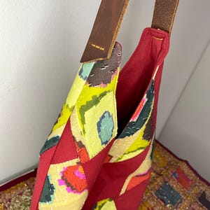 May include: A red patchwork tote bag with a brown leather strap. The bag is made of different fabrics with colourful patterns.