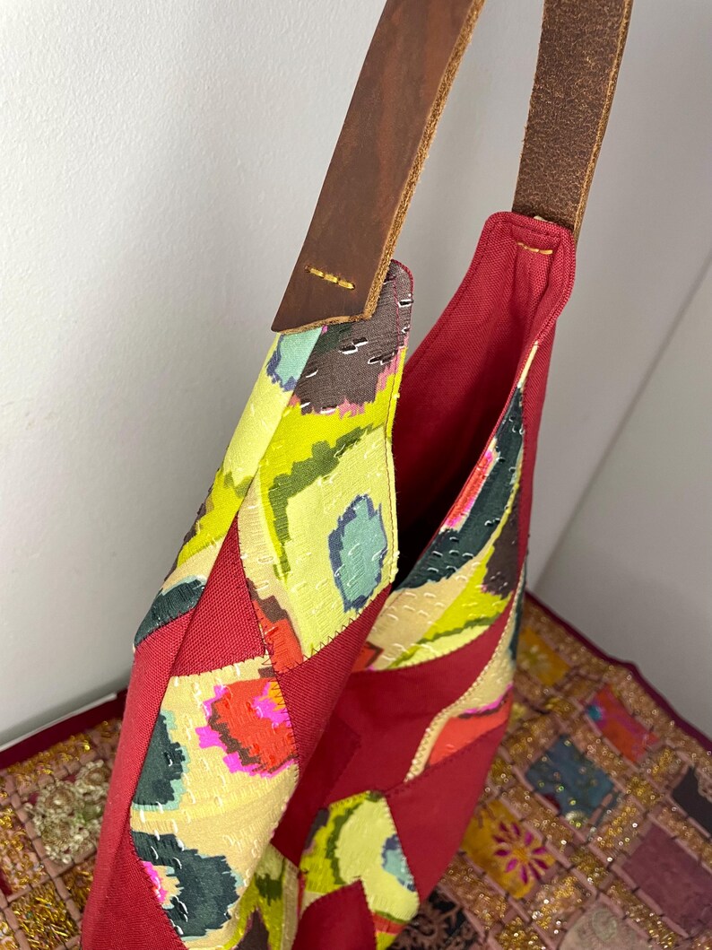 May include: A red patchwork tote bag with a brown leather strap. The bag is made of different fabrics with colourful patterns.