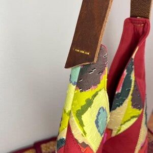 May include: A red, green and yellow patchwork tote bag with a brown leather strap. The bag has a geometric pattern and is made of different fabrics.