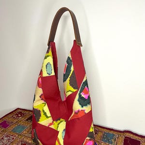 May include: A red patchwork tote bag with a brown leather strap. The bag is made of different fabrics with a colourful ikat pattern.