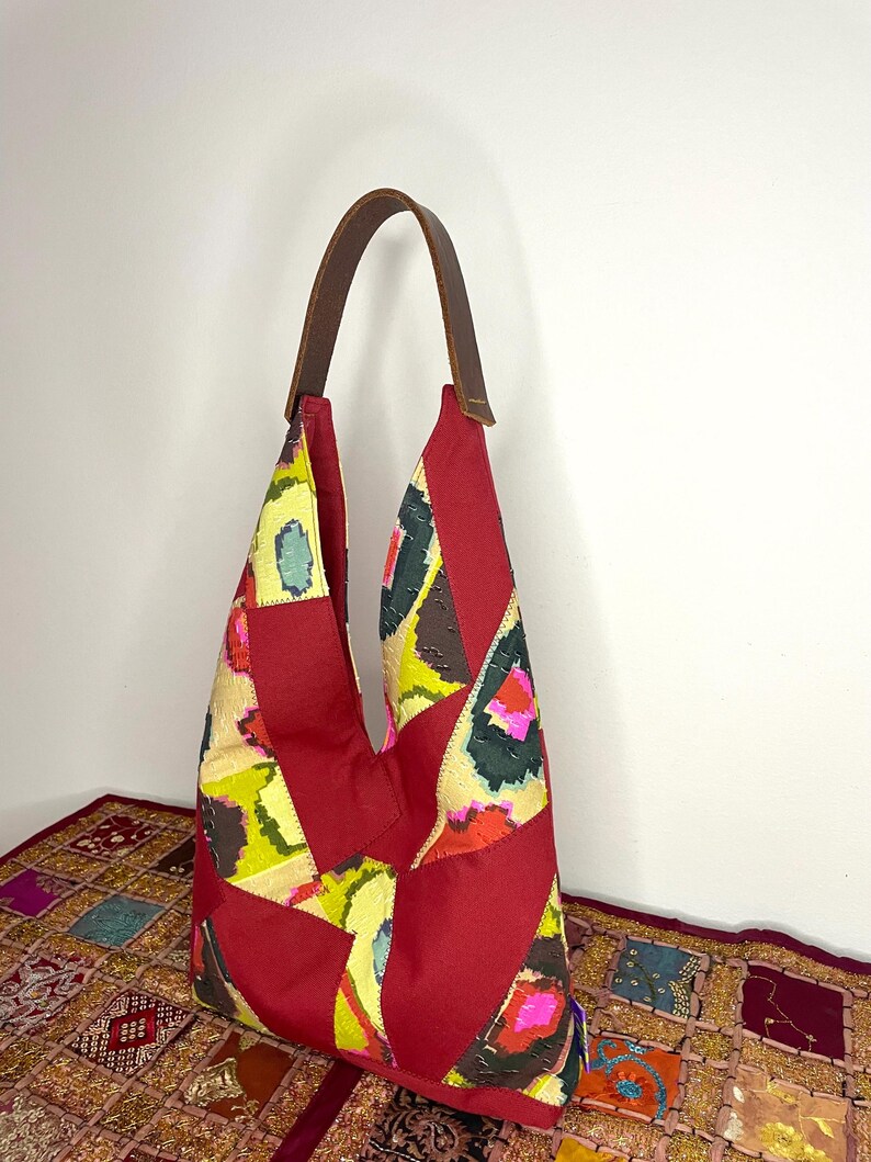 May include: A red patchwork tote bag with a brown leather strap. The bag is made of different fabrics with a colourful ikat pattern.