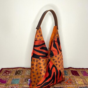 Pode incluir: Uma bolsa tote de couro marrom com um design de patchwork. A bolsa &eacute; feita de diferentes tecidos, incluindo uma estampa floral, uma estampa de zebra e um tecido preto. A bolsa tem uma &uacute;nica al&ccedil;a de couro marrom.