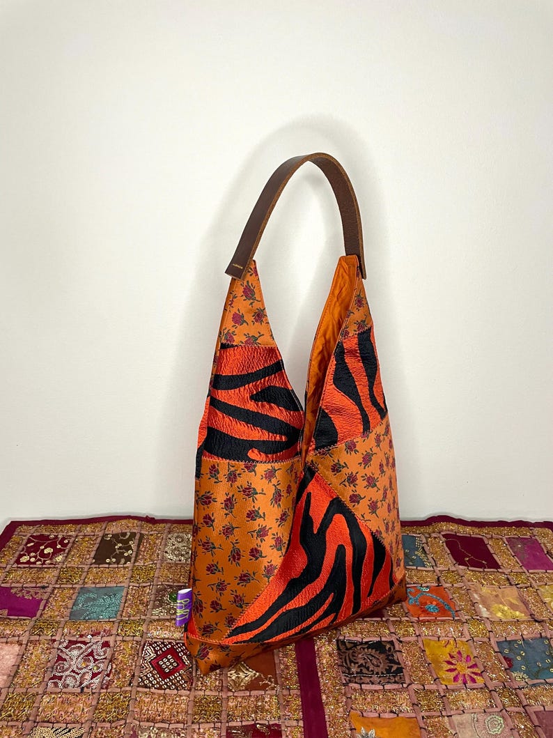 Pode incluir: Uma bolsa tote de couro marrom com um design de patchwork. A bolsa &eacute; feita de diferentes tecidos, incluindo uma estampa floral, uma estampa de zebra e um tecido preto. A bolsa tem uma &uacute;nica al&ccedil;a de couro marrom.