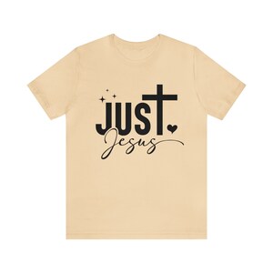 May include: A beige t-shirt with a black cross and the text "JUST Jesus" printed on the front.