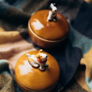 Unique pottery trinket box with black and white dog figurine sitting on orange crackle glazed lid, deep blue cup-style base, autumn home decor piece for storing rings and small treasures
