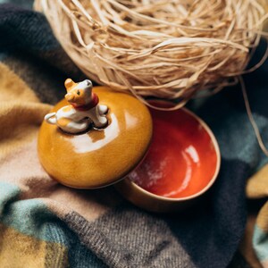 Small ceramic jewelry organizer box with charming spotted puppy sculpture on autumn-toned amber lid, displayed on rustic wood surface with soft textiles, cozy seasonal home decor aesthetic