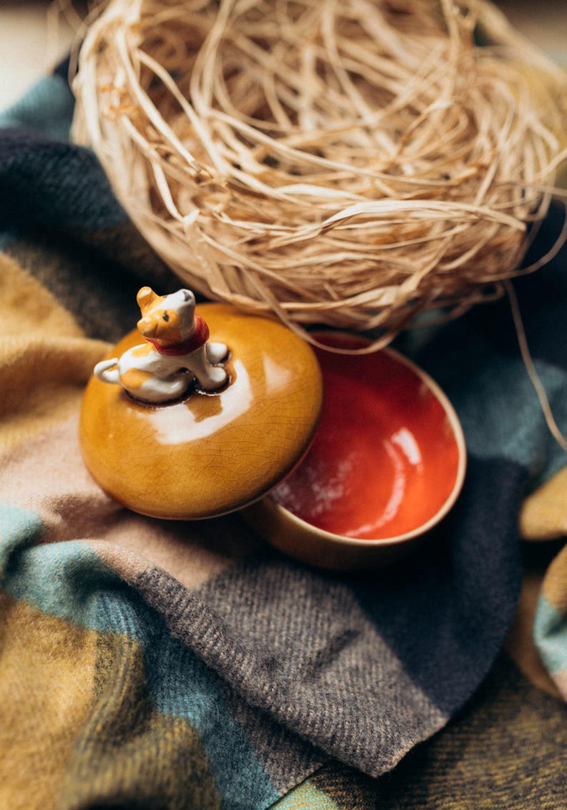 Small ceramic jewelry organizer box with charming spotted puppy sculpture on autumn-toned amber lid, displayed on rustic wood surface with soft textiles, cozy seasonal home decor aesthetic