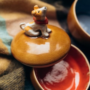 Handmade ceramic trinket box with warm amber crackle glaze lid topped by black and white spotted dog figurine, navy blue glossy base, autumn fall home decor, pet lover jewelry storage