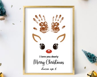 May include: A white framed print with a handprint reindeer design. The reindeer has brown antlers, black eyes, and a red nose. The text reads "I love you dearly Merry Christmas Lucas age 5".