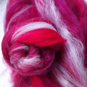 May include: A close-up of a bundle of pink and white wool roving. The wool is soft and fluffy, and it is perfect for spinning or felting.