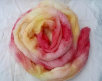 Puede incluir: Un ovillo de lana teñida a mano en tonos de amarillo, naranja y rosa. La lana está dispuesta en espiral, creando un efecto colorido y texturizado.