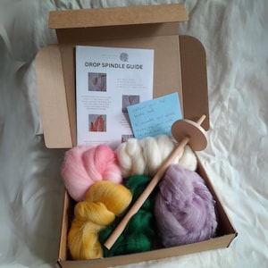 May include: A drop spindle kit containing a wooden spindle, a guide, and five different colours of wool roving: pink, white, yellow, green, and purple.