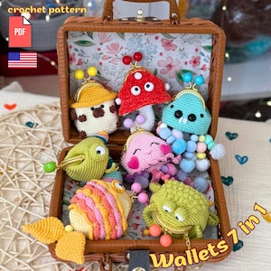 Op de afbeelding: Een bruine rieten koffer die zeven kleurrijke gehaakte munttasjes toont. De tasjes zijn gevormd als een paddenstoel, een vis, een vogel, een kwal en andere grillige wezens. De tekst "Wallets 7 in 1" is zichtbaar.