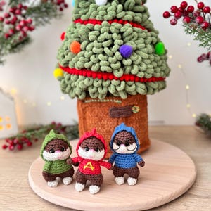 May include: A handmade Christmas tree with colorful ornaments and three small chipmunk figurines. The tree is green with red accents, and the chipmunks wear green, red, and blue sweaters. The figurines are on a wooden surface.