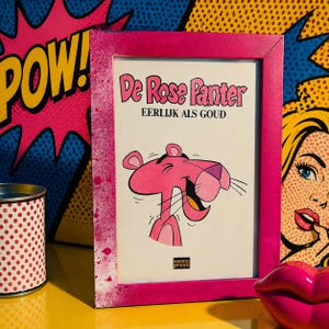Op de afbeelding: Een rechthoekige roze lijst met een stripboekcover getiteld De Rose Panter EERLIJK ALS GOUD. De cover bevat een cartoonillustratie van het personage de Roze Panter met een brede grijns. Het Semic Press logo staat onderaan afgedrukt.