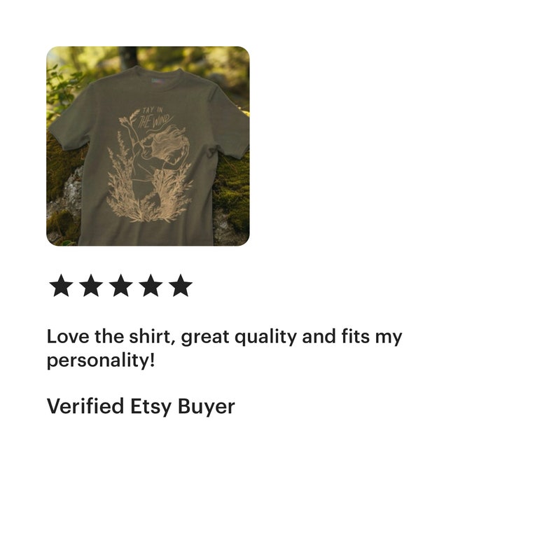 May include: An olive green short-sleeved t-shirt featuring a tan line-art graphic of a person with long hair standing amidst tall grasses. The text "TAY IN THE WIND" is printed in a stylized font above the figure on the front of the garment.