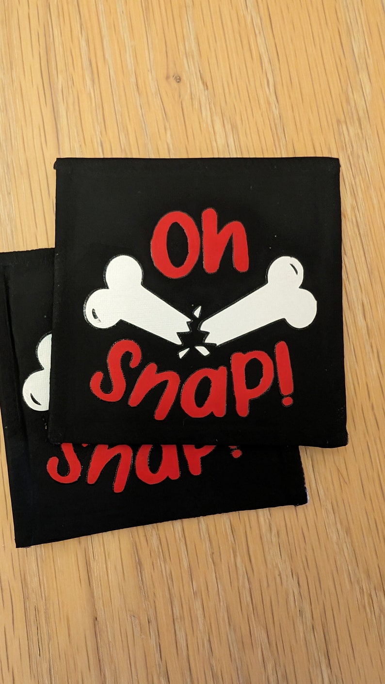 May include: Two black fabric patches with white bone designs and red text that reads "Oh Snap!" and "Snap!"