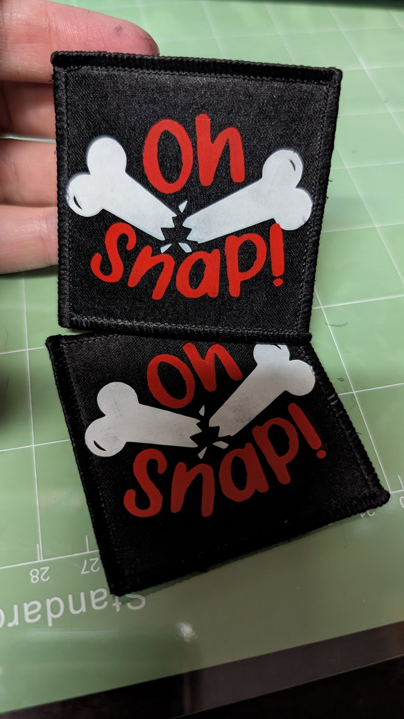 May include: Two black fabric patches with white bone designs and red text that reads "Oh Snap!"