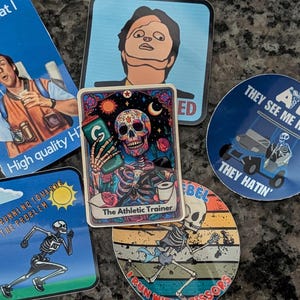 Peut inclure: Plusieurs autocollants colorés avec des motifs variés. L'un représente un squelette en course, un autre un crâne avec une boisson, et d'autres affichent du texte comme "They See Me Rollin'" et "That's what I call".