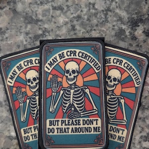 May include: Three rectangular patches with a skeleton illustration. The patches have the text "I MAY BE CPR CERTIFIED BUT PLEASE DON'T DO THAT AROUND ME". The background features a sunburst design with red, orange, and blue colors.