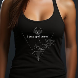 May include: Black tank top with a white graphic of a hand holding a glowing orb with an eye inside a triangle. The text "I put a spell on you" is printed below the graphic.
