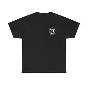 May include: Black t-shirt with a small emblem on the upper left chest. The emblem is a shield shape with the words "SQUAD 31. RIVER" in white and red lettering. The shirt is a crew neck style.