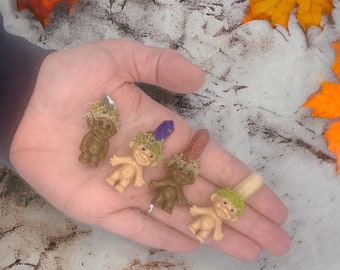 May include: Five miniature troll figurines with moss and crystal accents. The trolls are made of plastic and have a whimsical, handmade aesthetic.