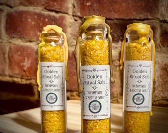 May include: Three small glass bottles filled with yellow crystals and sealed with a gold wax. Each bottle has a white label with the text "Golden Ritual Salt" and "For Happiness & Positive Energy".