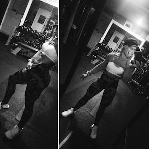 May include: A woman wearing a black and white patterned top and leggings poses in a gym. She is wearing a black hat and has a confident expression.