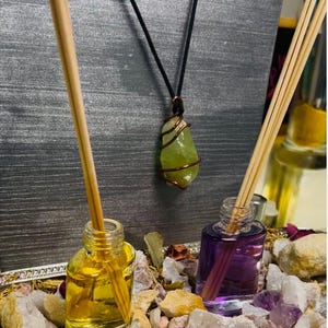 May include: Two small glass bottles with clear liquid and wooden sticks, one yellow and one purple, sitting on a tray with white and brown rocks. A green stone wrapped in copper wire hangs from a black cord.