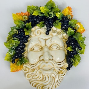 Peut inclure: Un masque en céramique blanche avec une barbe détaillée et une couronne de feuilles vertes et de raisins noirs.