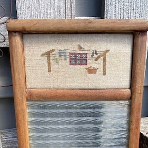 Puede incluir: Una ventana de cristal ondulado con marco de madera vintage con un diseño de punto de cruz de pájaros en un tendedero. El diseño de punto de cruz está sobre una tela de lino beige.