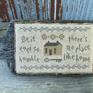 May include: A framed cross-stitch sampler with the text "Be it ever so humble there's no place like home". The sampler features a small house with a key and a border of small flowers.